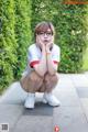 A woman wearing glasses crouching down on a sidewalk.