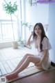 A woman sitting on a wooden floor next to a window.