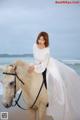 A woman in a white dress riding a white horse on the beach.