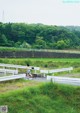 A woman walking across a bridge over a grassy field.