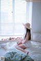 A woman sitting on a bed in front of a window.