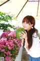 A young woman holding a watermelon in front of flowers.