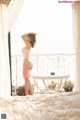 A woman in a pink bikini standing on a bed.