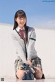 A young woman in a school uniform sitting on the ground.